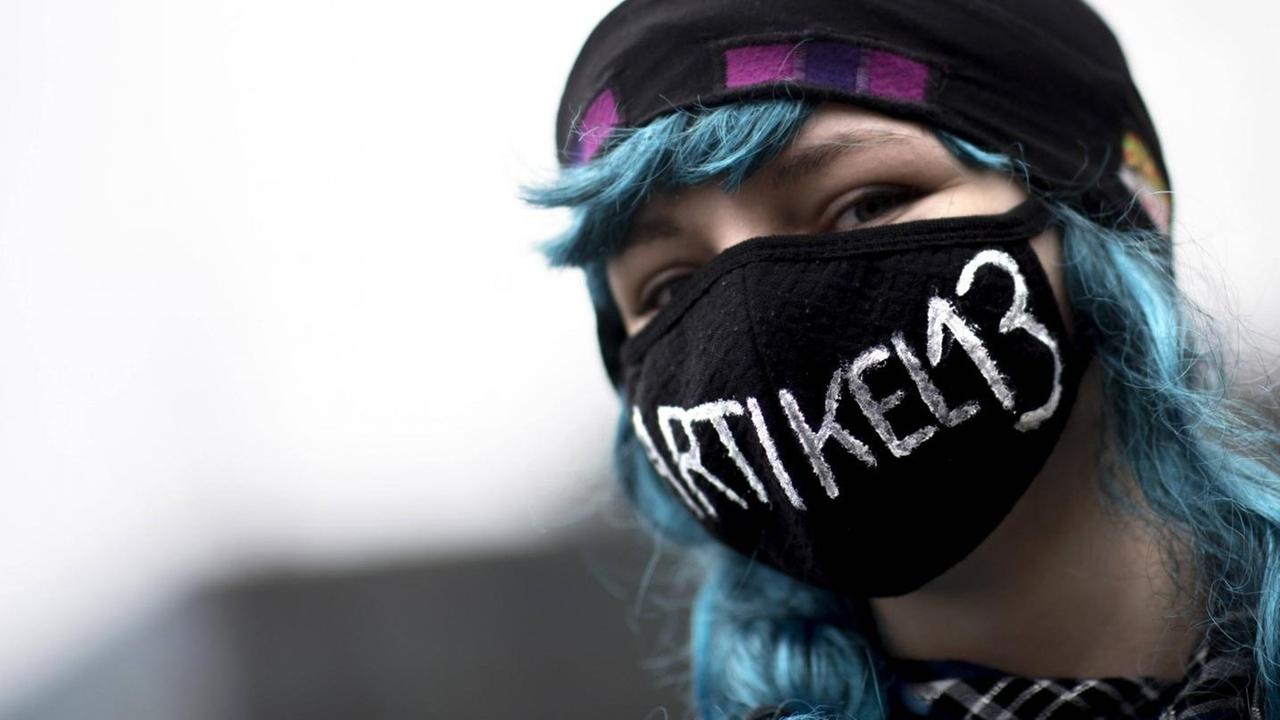 Eine junge Demonstrantin protestiert in Berlin gegen die EU-Urheberrechtsreform. Sie trägt einen Mundschutz, auf dem "Artikel 13" steht.