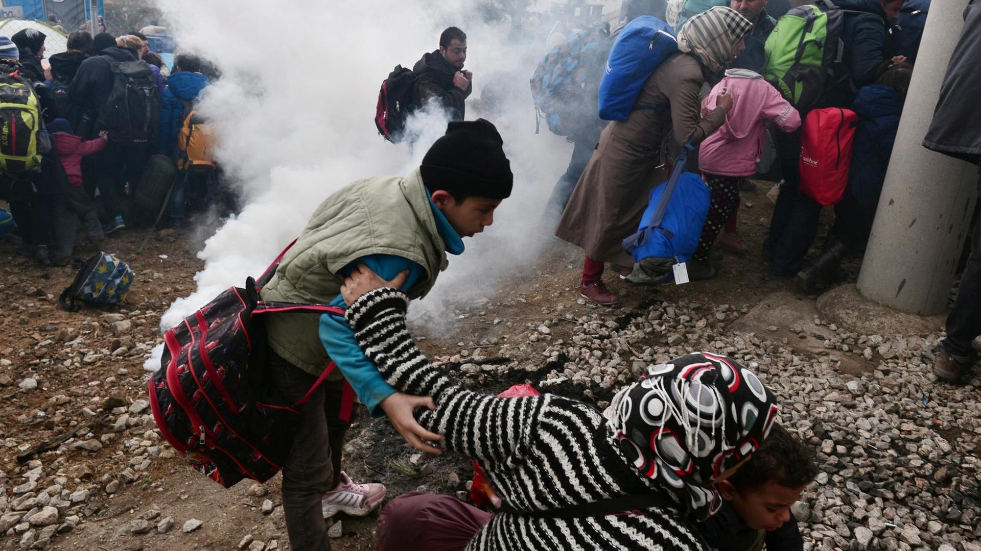 Aus einer Patrone strömt dichtes weißes Gas. Flüchtlingen fliehen, Eltern ziehen ihre Kinder aus der Dunstwolke. Aus einer Patrone strömt dichtes weißes Gas. Flüchtlingen fliehen, Eltern ziehen ihre Kinder aus der Dunstwolke.