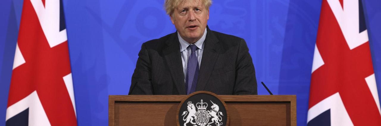 Großbritanniens Premier Boris Johnson steht neben Flaggen am rednerpult und informiert über die Corona-Maßnahmen.