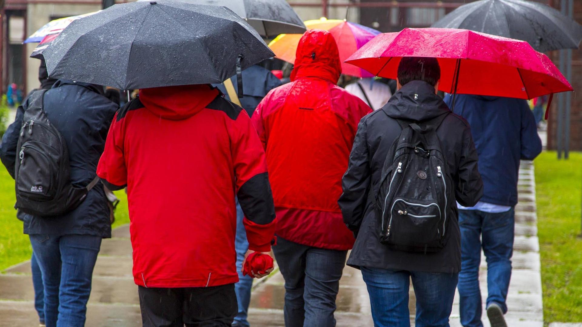 Menschen bei Regenwetter, in Regenkleidung, mit Regenschirmen.