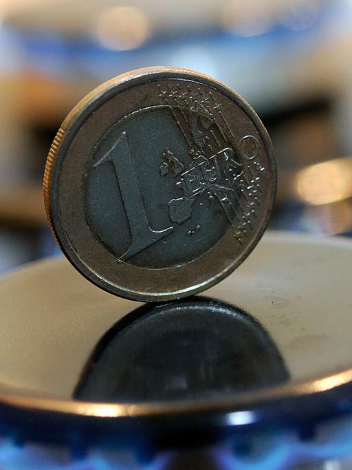 Eine Ein-Euro-Münze steht zwischen den Flammen einer mit Gas betriebenen Kochfläche.