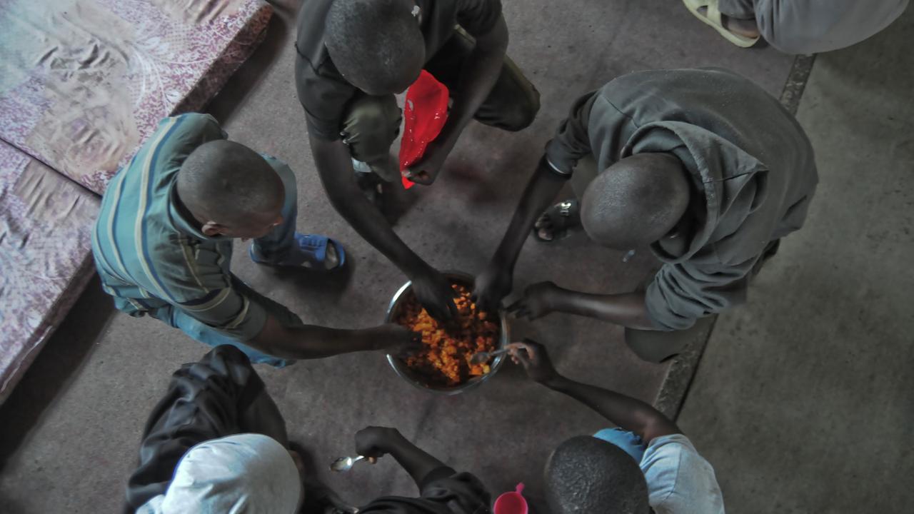 Afrikanische Geflüchtete knien am 5.04.2017 in einem Flüchtlingslager in Tripolis (Libyen) um eine Schale mit Essen.