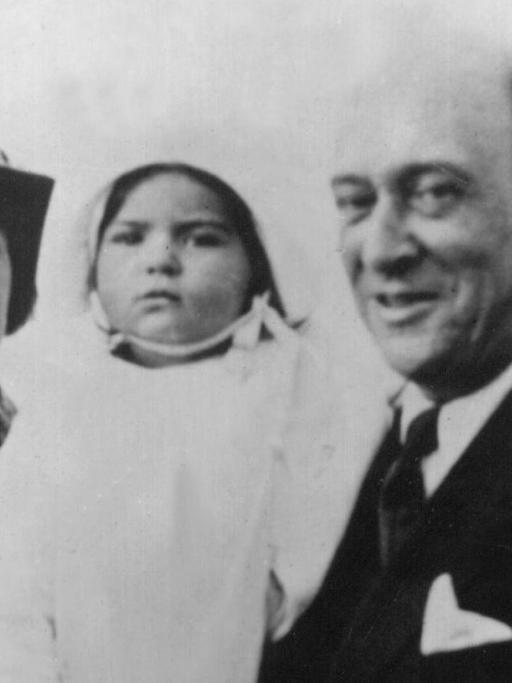 Eine historische Fotografie zeigt einen Mann mit Frau und Kind glücklich in die Kamera lächelnd.