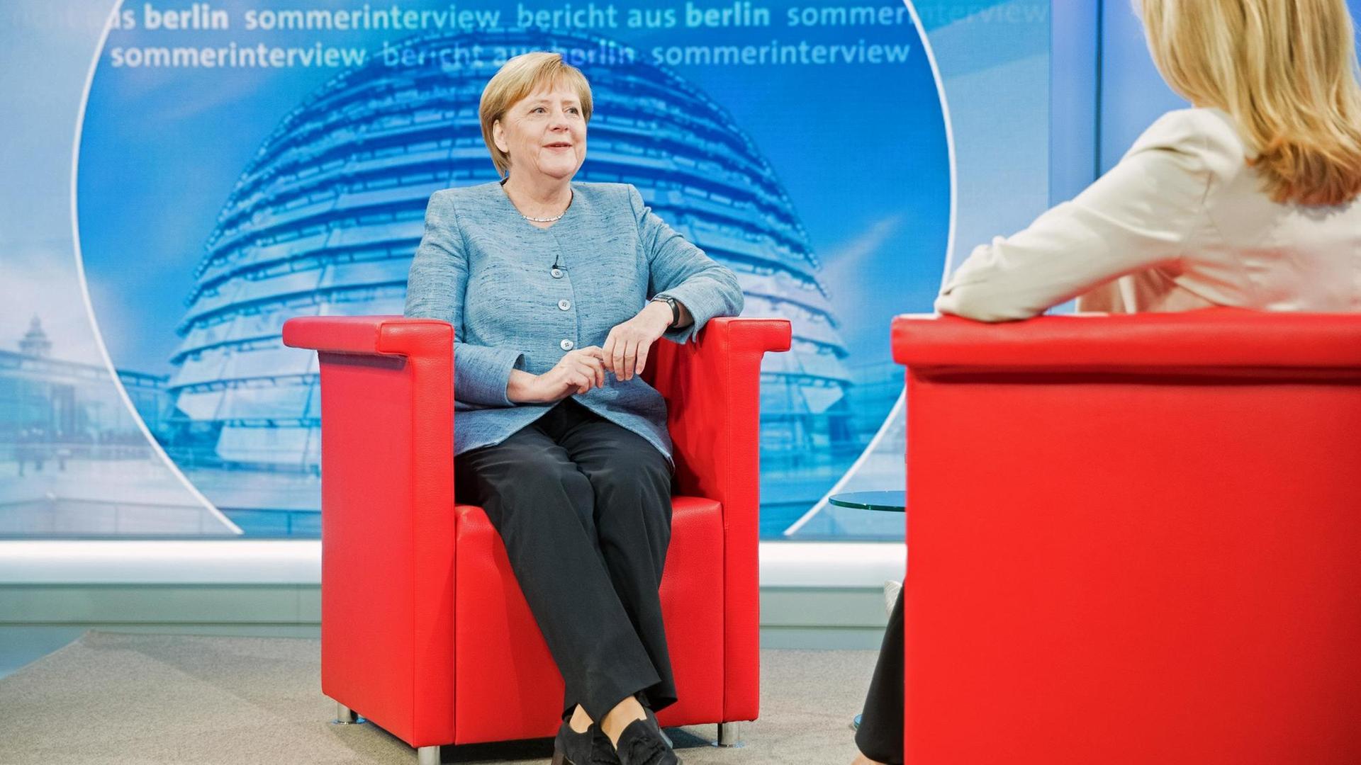 Bundeskanzlerin Merkel sitzt vor Beginn des ARD-Sommerinterviews in einem roten Sessel, ihr gegenüber mit dem Rücken zur Kamera sitzt Studioleiterin Tina Hassel.