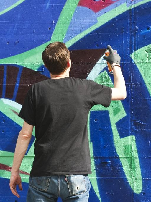 Ein Sprayer schreibt einen Schriftzug an eine Wand