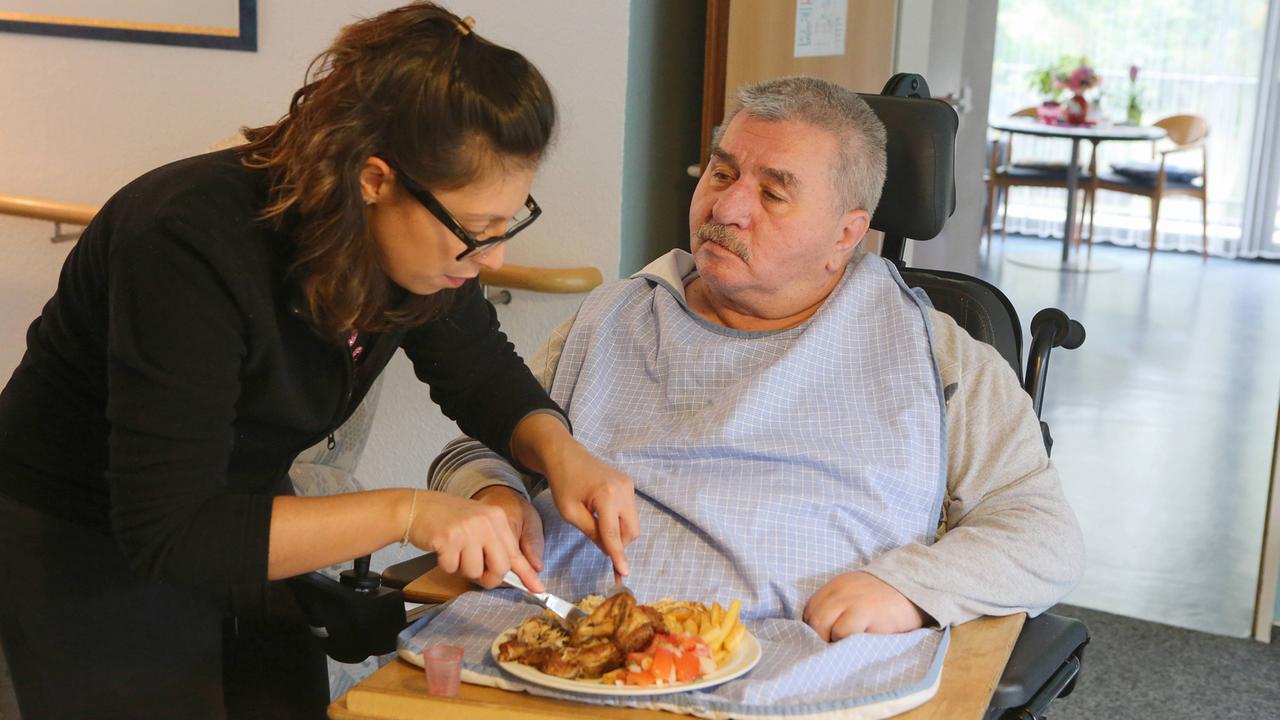 Eine Mitarbeiterin schneidet einem Pflegebedürftigen das Essen zurecht - hier im Multikulturellen Seniorenzentrum des Deutschen Roten Kreuzes, Haus am Sandberg, in Duisburg