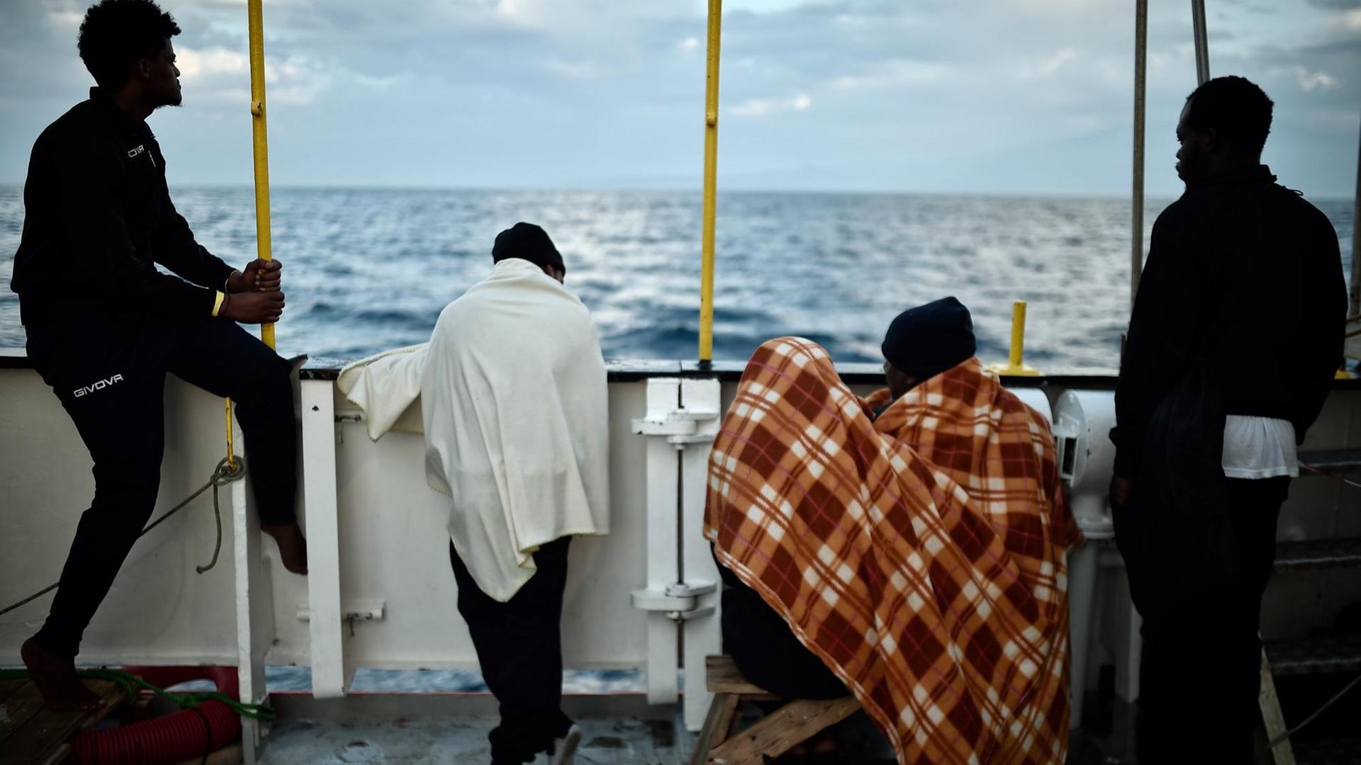 Afrikaner stehen an der Reling eines Schiffes, mit dem Rücken zur Kamera.