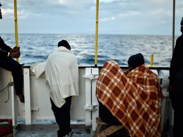 Afrikaner stehen an der Reling eines Schiffes, mit dem Rücken zur Kamera.