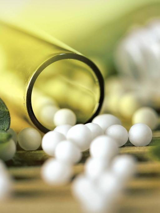 Globuli, ein homöopathisches Mittel, kleine Perlen und Pflanzenblätter liegen auf einem Tisch.