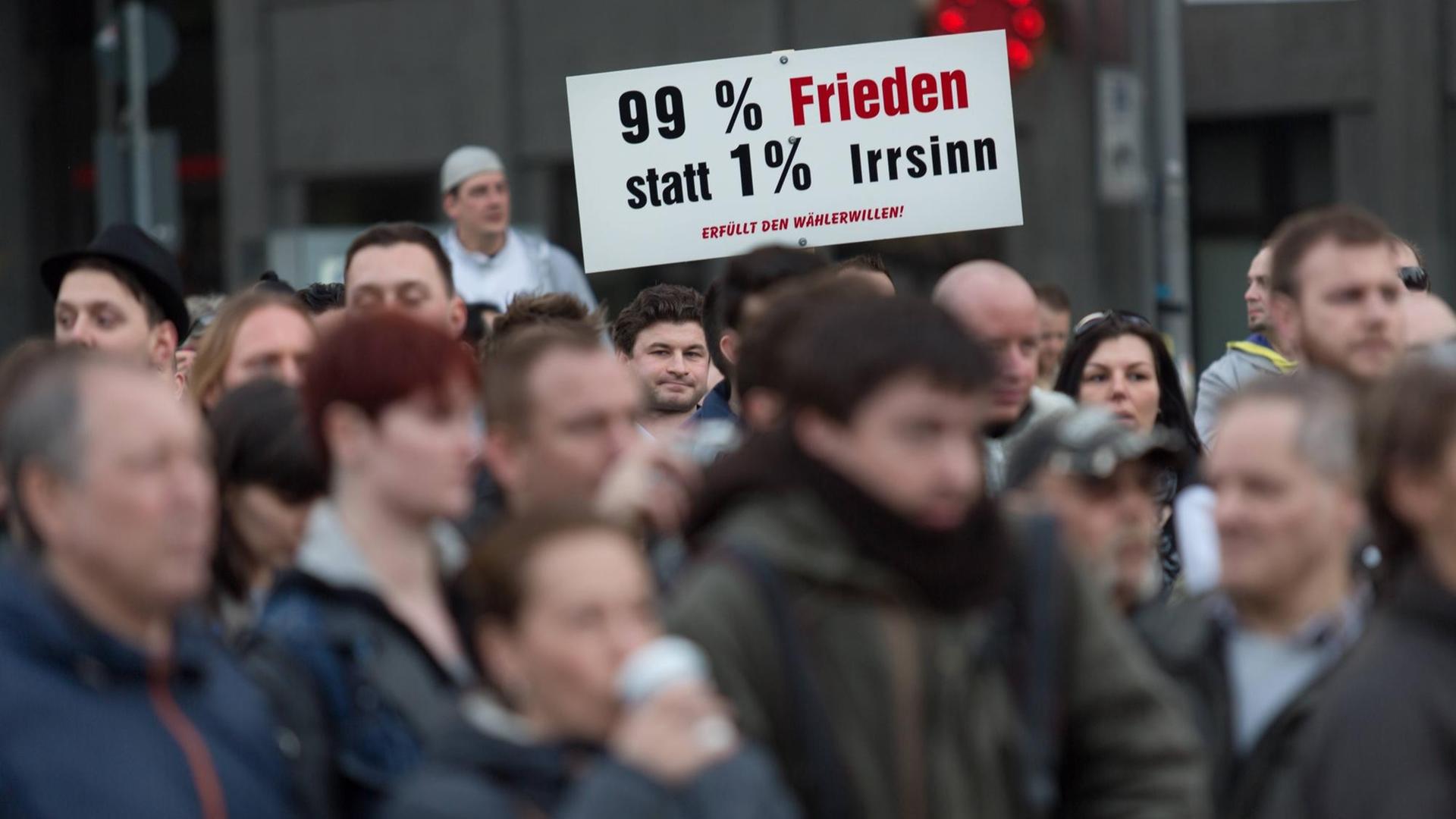Eine Menschenmenge steht am 31.3.2014 zusammen und hält ein Schild hoch, auf dem "99% Frieden statt 1% Irrsinn - Erfüllt den Wählerwillen" geschrieben steht.