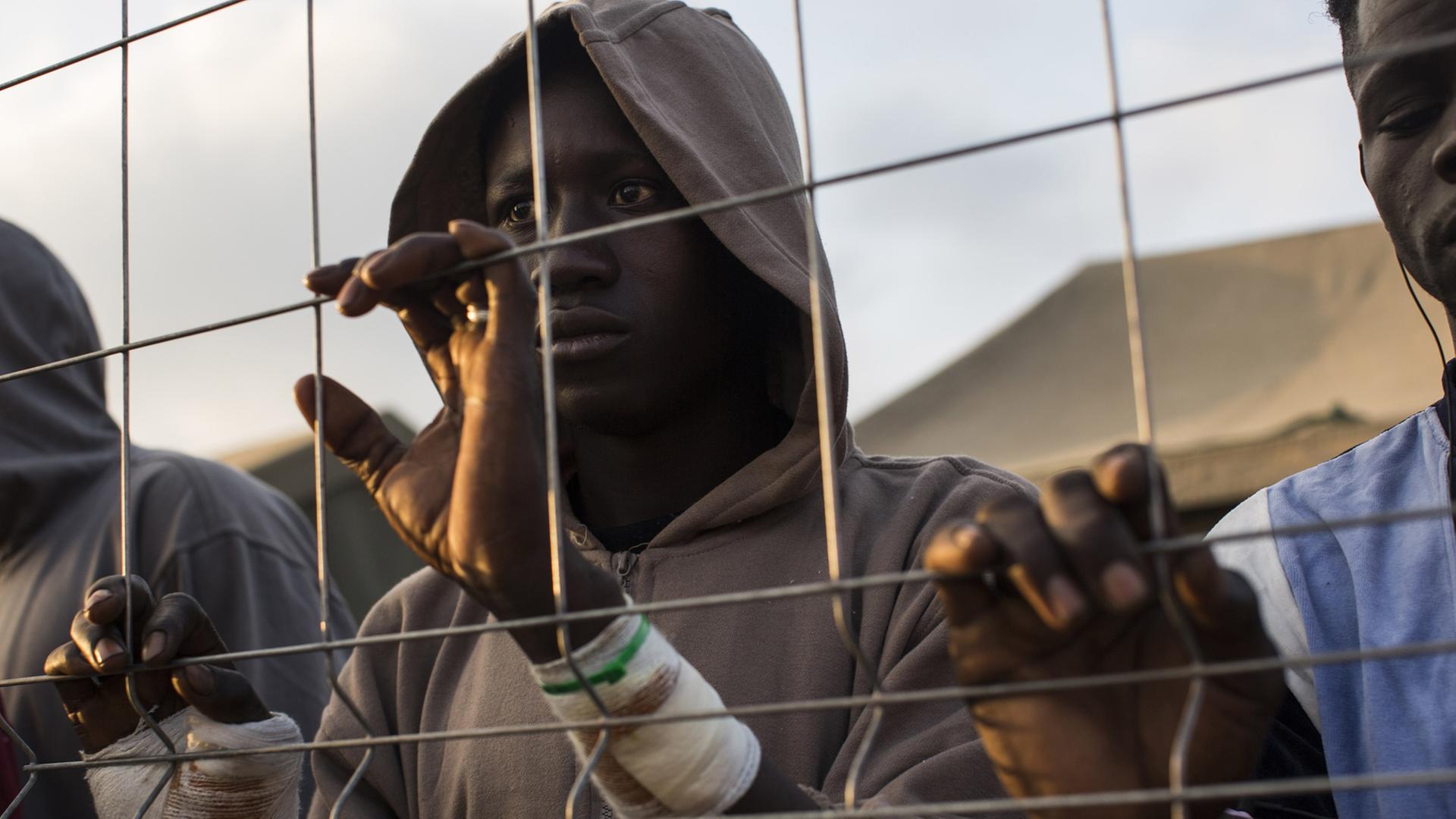 Ein Flüchtling schaut durch einen Grenz-Zaun.