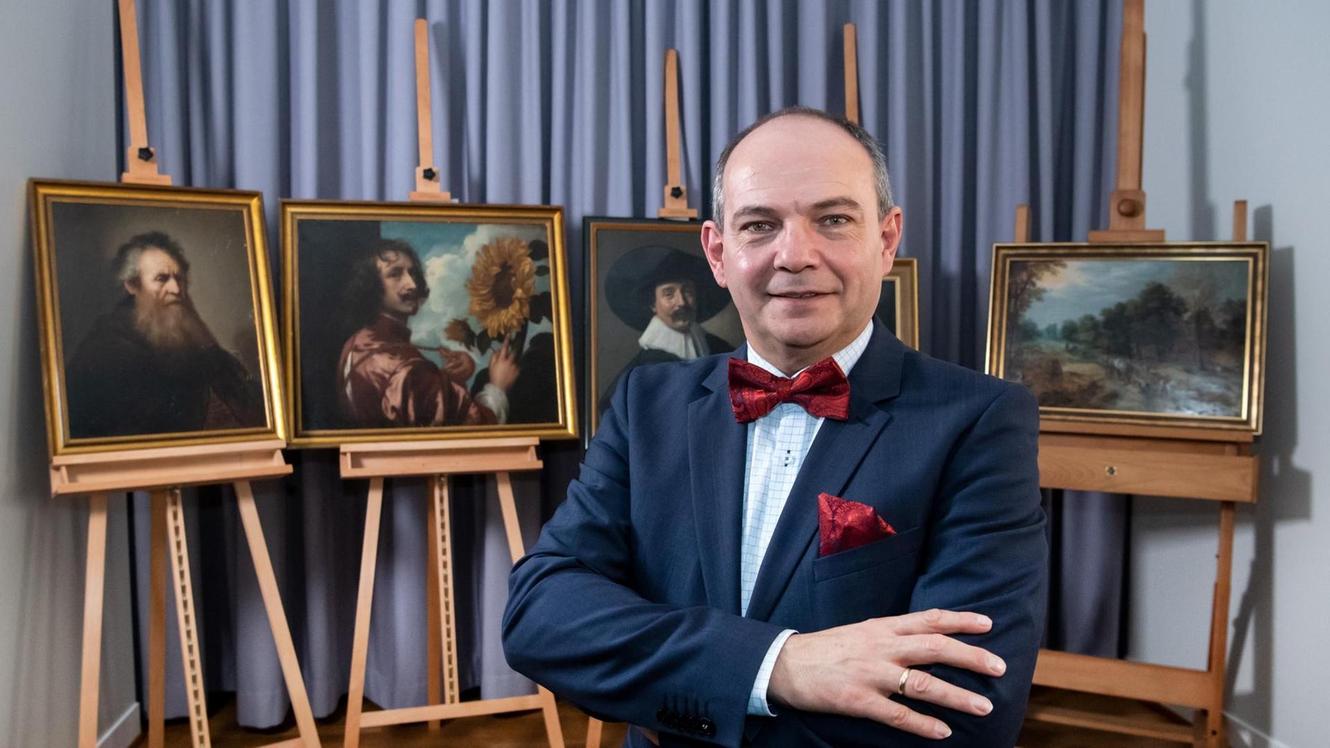Der Bürgermeister von Gotha, Knut Kreuch, steht mit vor der Brust verschränkten Armen vor fünf vormals vermissten Gemälden.