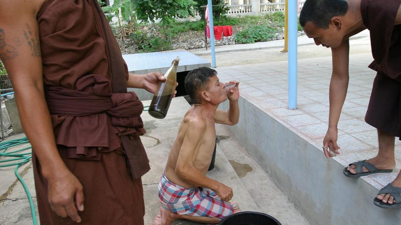 Ein Drogenabhängiger trinkt ein von Mönchen selbstgebrautes und pflanzliches Erbrechungsgetränk. Für die Prozedur gibt es im Wat Thamkrabok Kloster spezielle "Erbrechungsbereiche" mit Abflussrinnen.