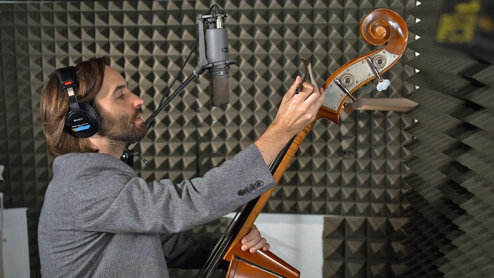 Der Musiker und Komponist Gregor Schwellenbach stimmt mit Kopfhörern einen Kontrabass
