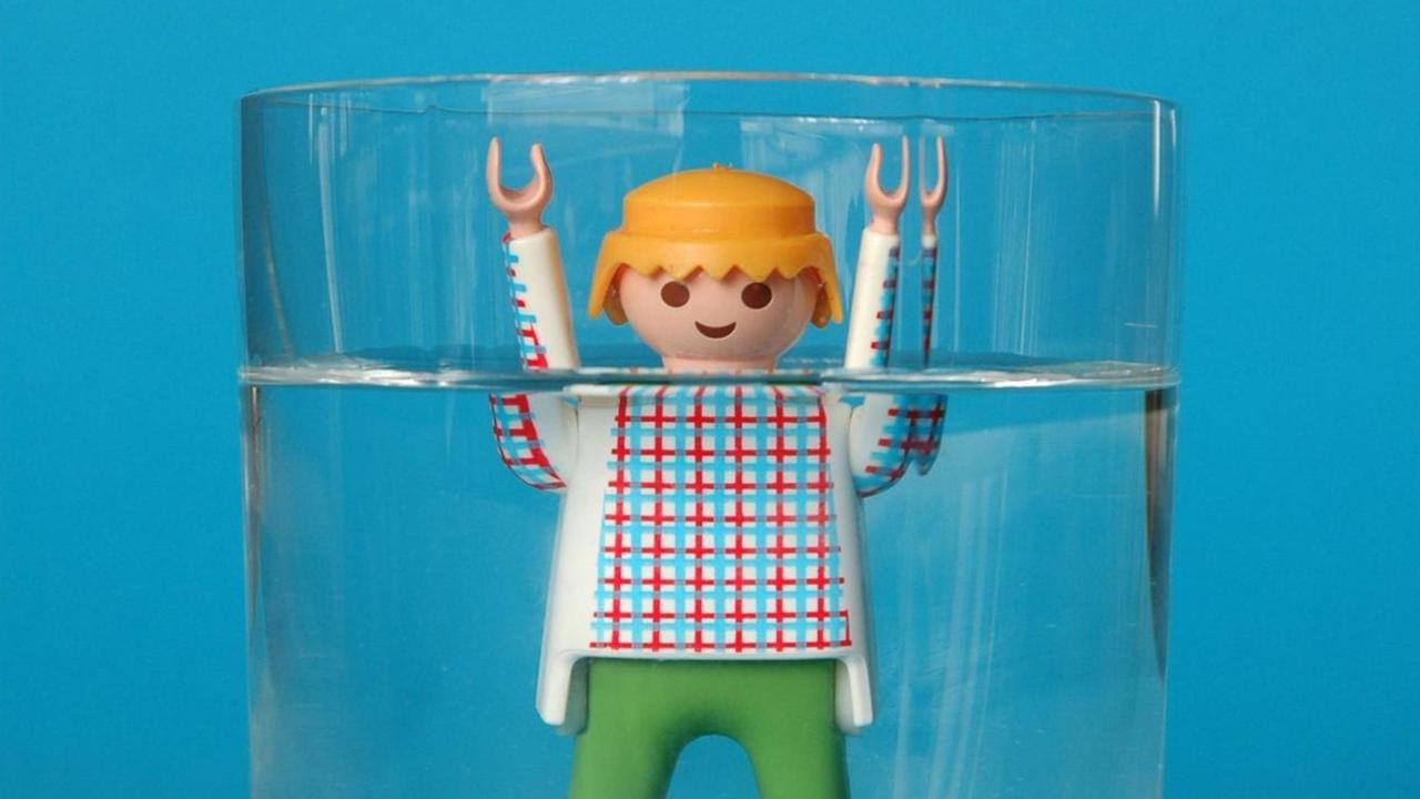 Eine kleine Figur steht bis zum Hals in einem gefüllten Wasserglas.