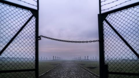 Sonnenaufgang im Morgennebel vor den halb offenen Drahttoren des Vernichtungslagers Auschwitz-Birkenau in Oswiecim, Polen.