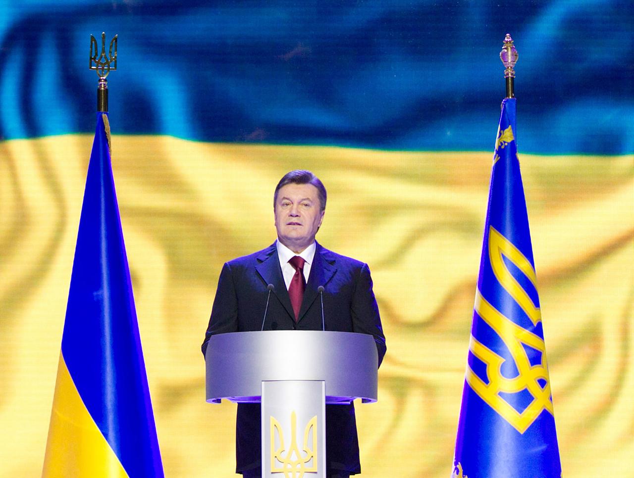 Der ukrainischen Präsident Viktor Janukowitsch steht flankiert von zwei blau-gelben Fahnen an einem Rednerpult.