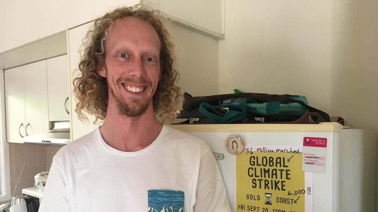 Zu sehen ist ein Mann mit längeren, blonden Locken, der vor einem Kühlschrank steht. Am Kühlschrank hängt ein Plakat, was auf den Global Klimastreik an der Gold Coast in Australien aufmerksam macht.