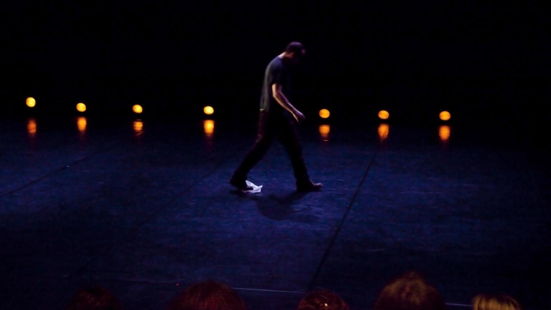 Ein Bühnenarbeiter trocknet mit einen Tuch am Fuß die schweiß getränkte Bühne nach einer Tanz-Performance.