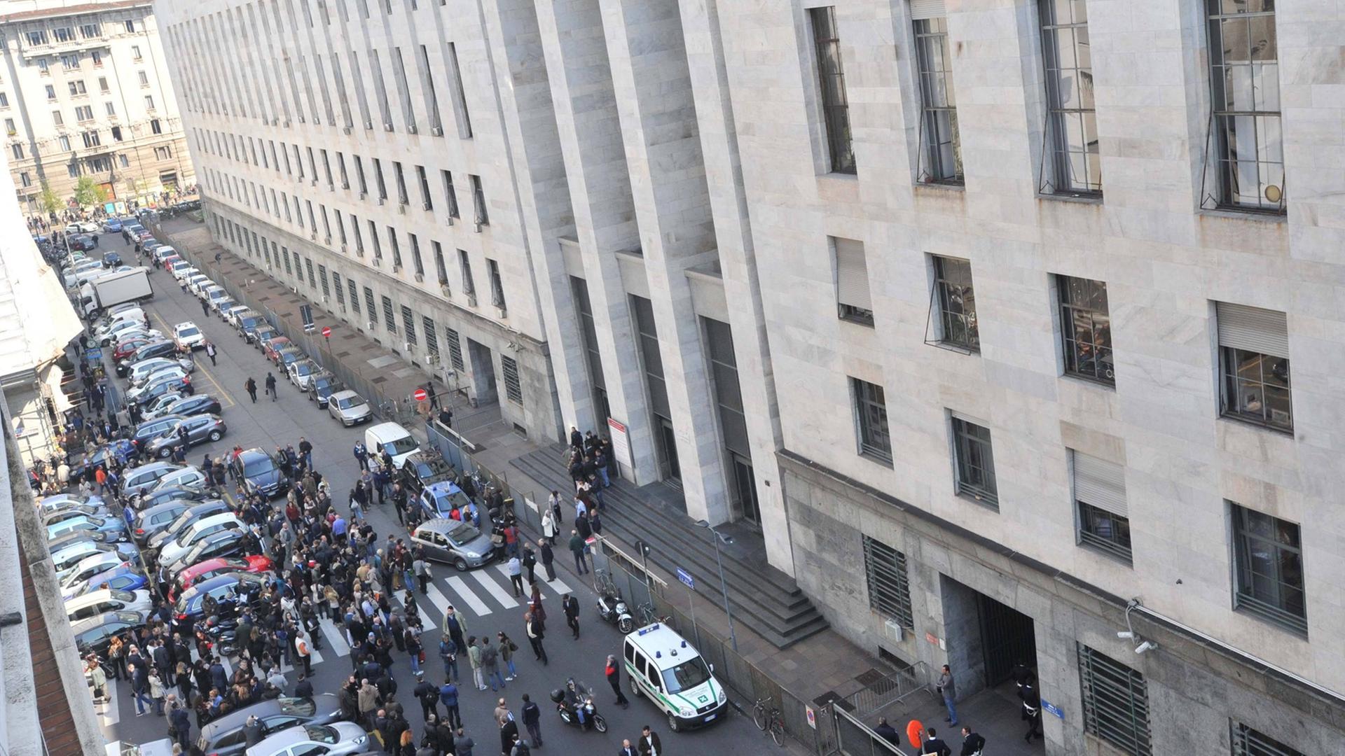 Der Mailänder Justizpalast von halb oben fotografiert, davor eine Menschenmenge und Polizeifahrzeuge.