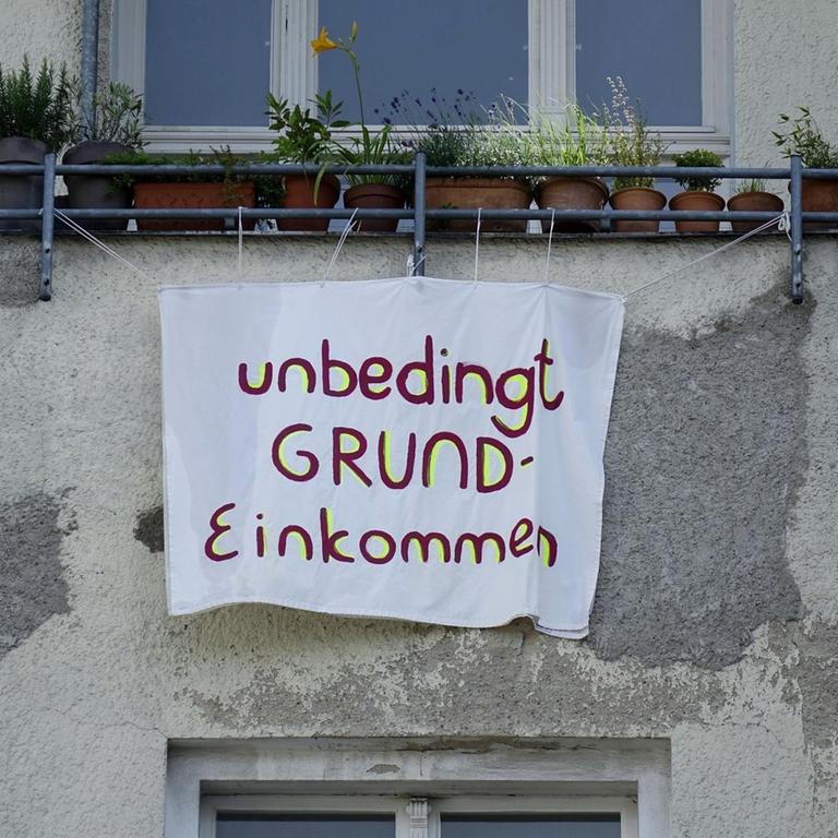 An einer Hausfassade in Berlin-Kreuzberg hängt ein Transparent, auf dem das Grundeinkommen gefordert wird.