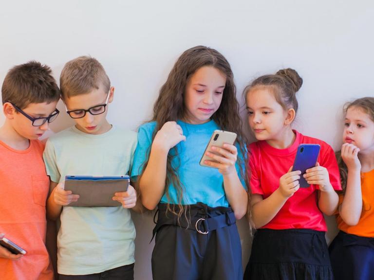 Schulmädchen und Schuljungen in bunten T-Shirts, schauen während der Pause auf ihre Smartphones.