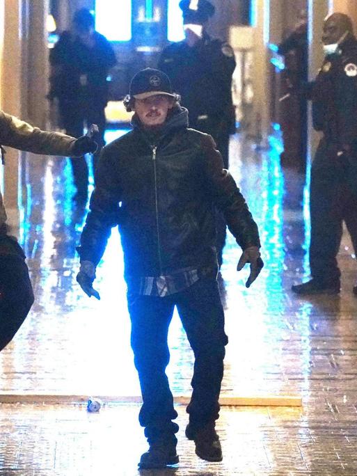 Zwei Protestler, die ins Kapitol eingedrungen sind, laufen auf die Kamera zu. Im Hintergrund stehen Polizisten.