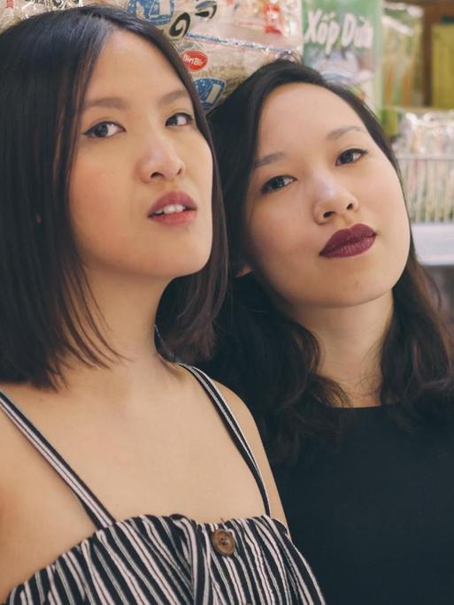 Vanessa Vu (rechts) und Minh Thu Tran (links) lehnen an einem Supermarkt-Regal mit asiatischen Lebensmitteln.