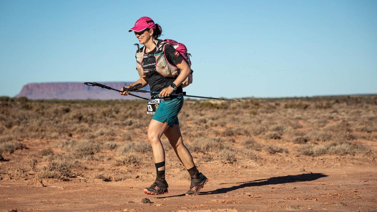 Eine Läuferin ist im australischen Outback zu sehen, im Hintergrund der Uluru.