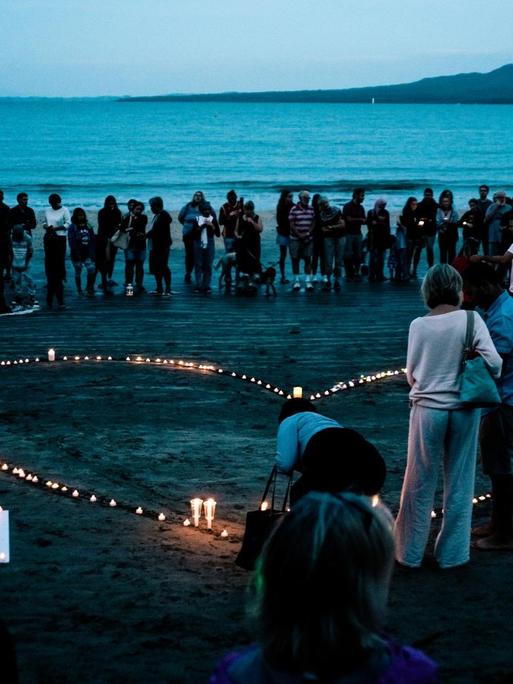 Eine Gruppe Menschen steht am Strand von Auckland in Neuseeland um ein Herz aus Kerzen.