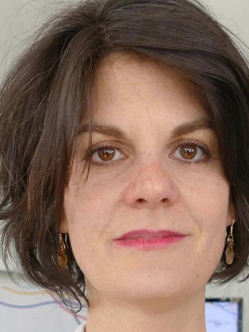 Eine junge Frau mit dunklen halblangen Haaren schaut in die Kamera.