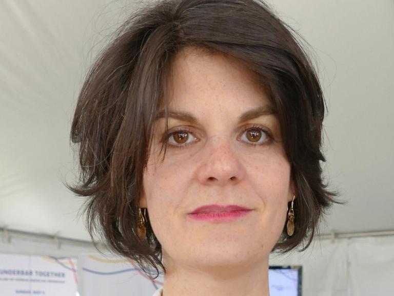 Eine junge Frau mit dunklen halblangen Haaren schaut in die Kamera.