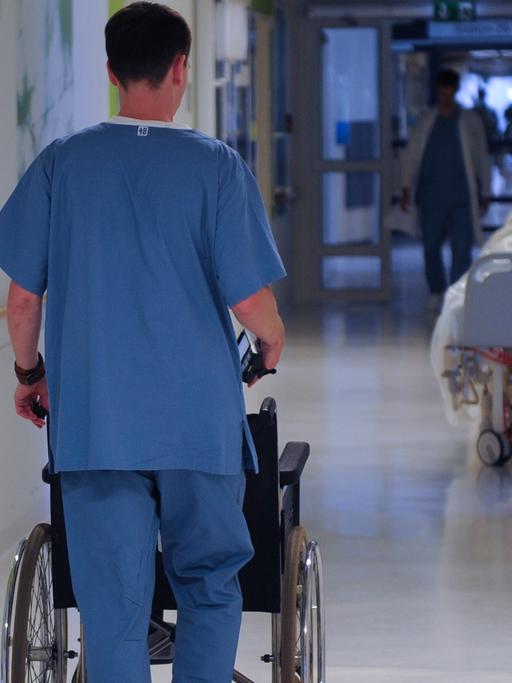 Ein Pfleger schiebt einen Rollstuhl durch einen Krankenhausflur.