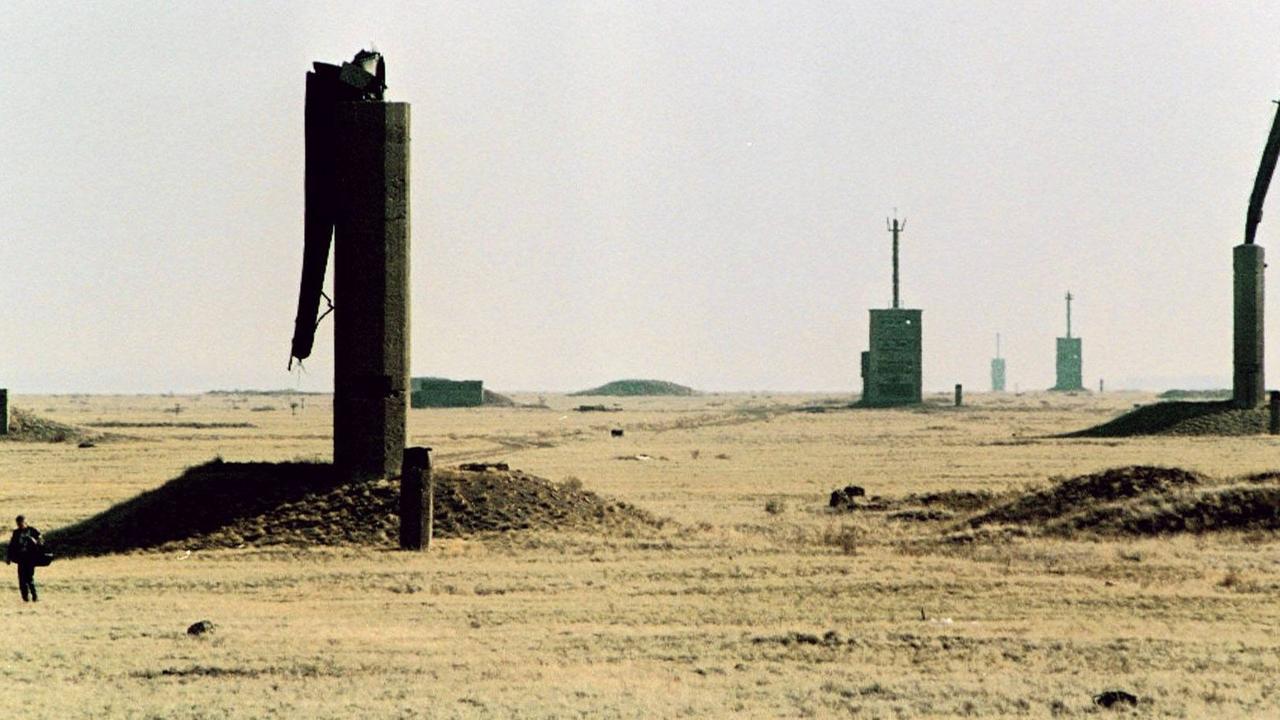 Ein Mann steht vor einer Wüstenlandschaft mit abgeknickten Metall-Türmen im ehemaligen Atomwaffen-Testgelände der UdSSR in Semipalatinsk, Kasachstan  