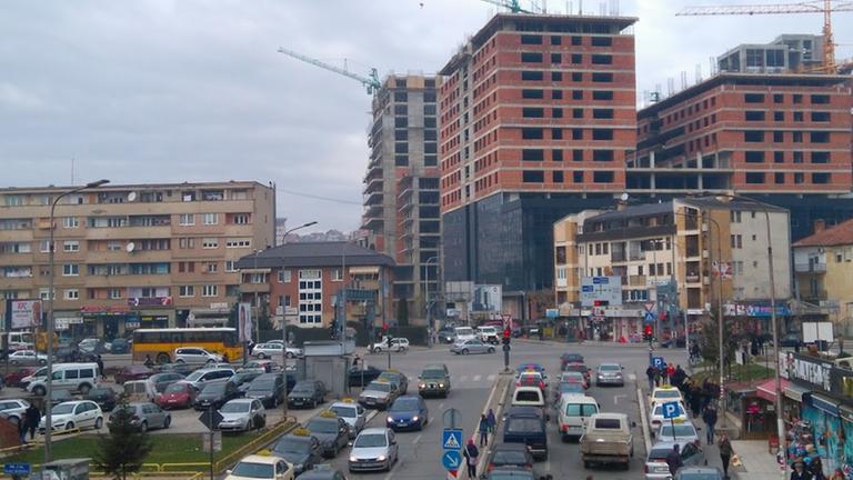 Hochhäuser am Rande Pristinas werden gebaut. Die Straße ist voll mit Autos.