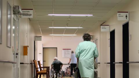 Eine Patientin wird in einem Rollstuhl über einen Krankenhausflur geschoben. 