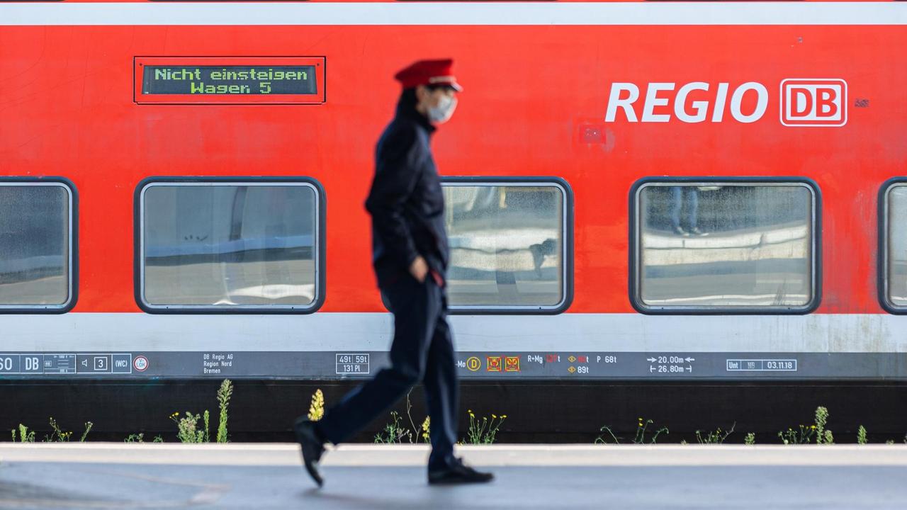 Ein Mitarbeiter der Deutschen Bahn läuft auf einem Bahnsteig in Hannover und ein Zug der DB Regio steht auf einem Gleis dahinter.
