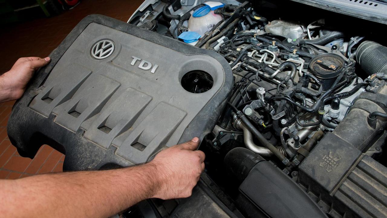 Ein KFZ-Servicetechniker mit einer Abdeckung vor einem vom Abgas-Skandal betroffenen 2.0l TDI Dieselmotor vom Typ EA189 in einem VW Touran in einer Autowerkstatt