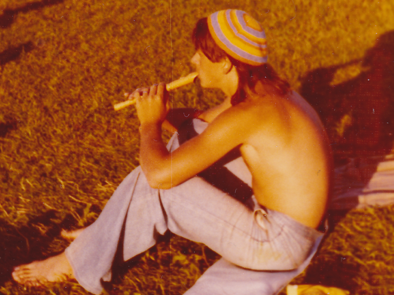 Ein junger Mann mit nacktem Oberkörper sitzt im Sommer 1974 auf dem Deich von Cuxhaven-Döse und spielt Flöte.