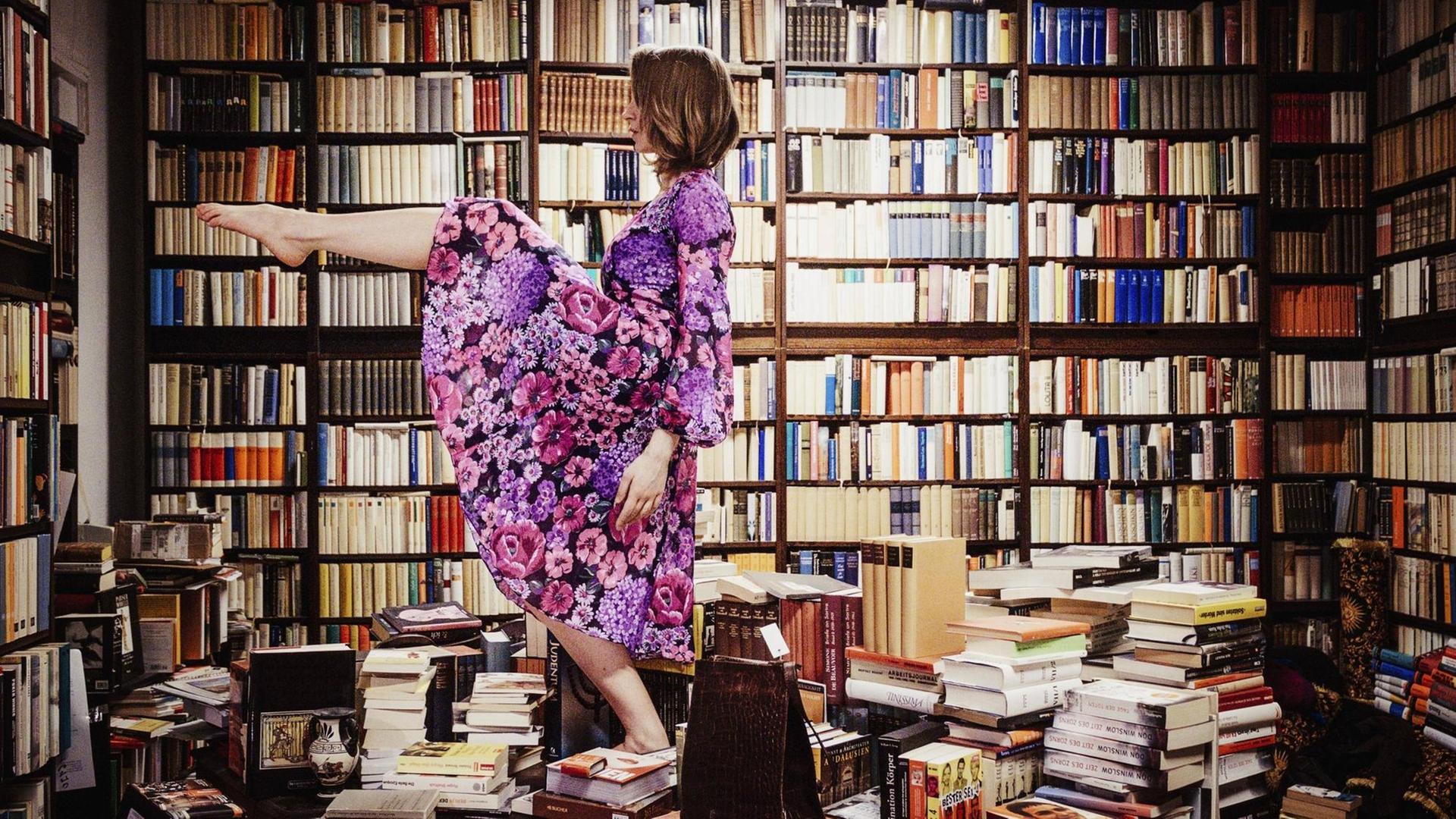 Eine Frau tanzt auf einem Stapel von Bücher mitten in einer Bibliothek.
