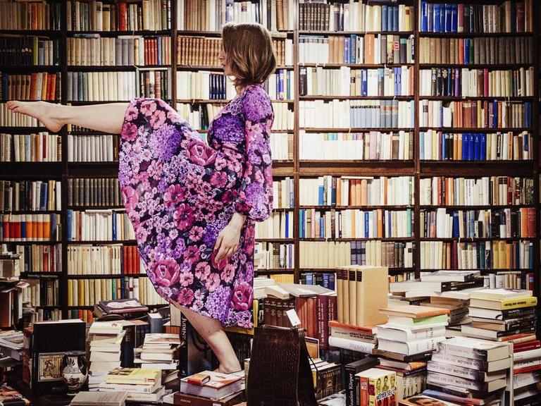 Eine Frau tanzt auf einem Stapel von Bücher mitten in einer Bibliothek.