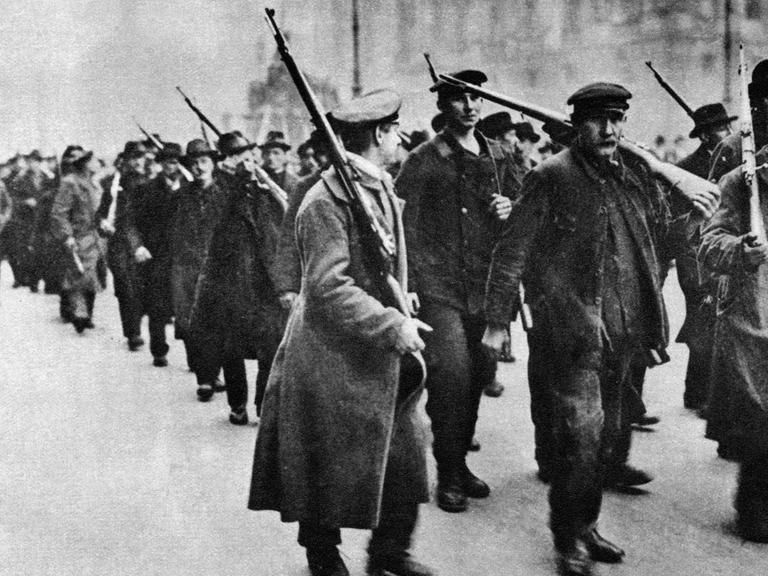 Das Schwarz-Weiß-Foto von 1918 zeigt, wie Aufständische im Zug der Novemberrevolution durch die Straßen Berlins ziehen.