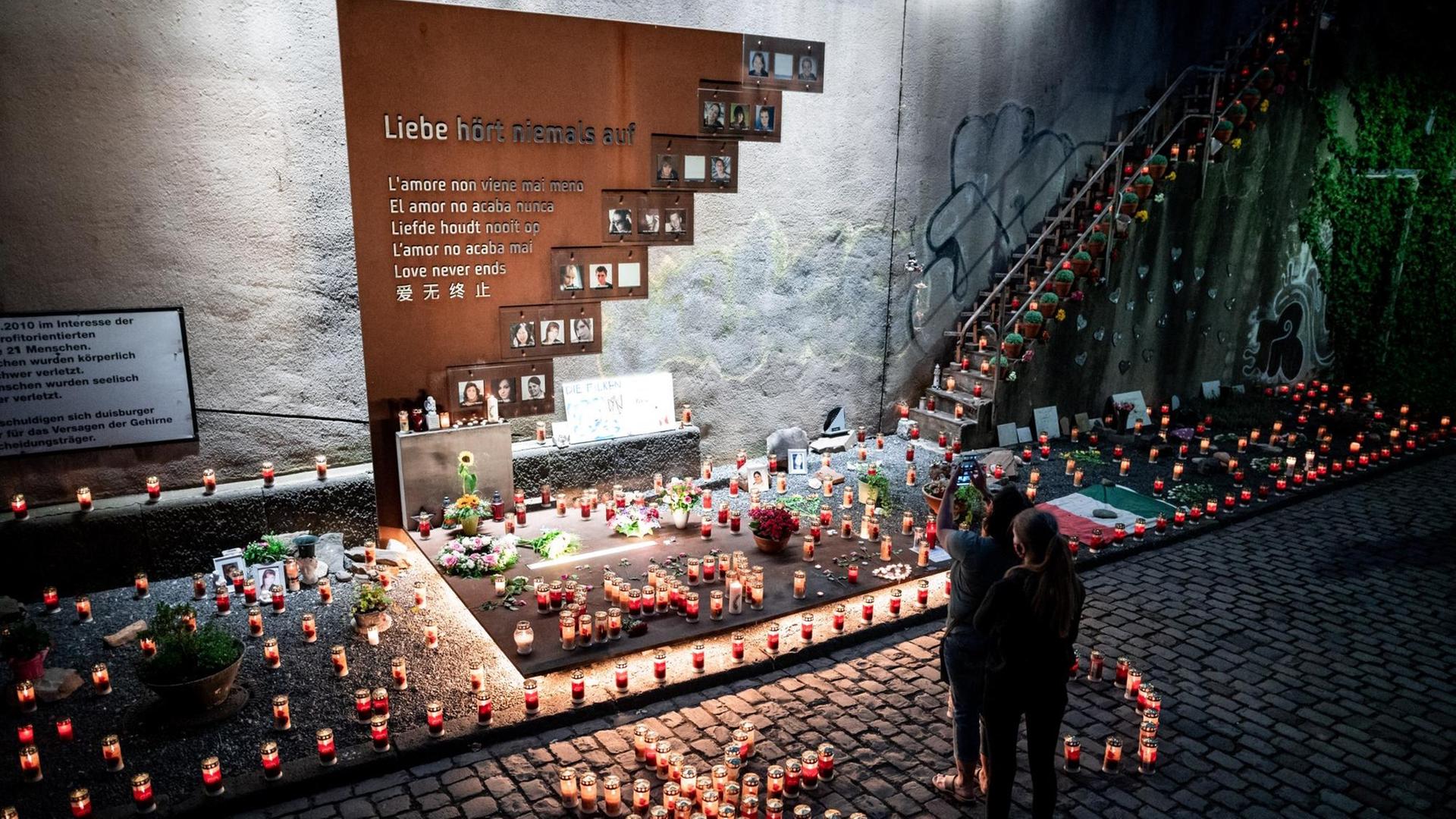 Menschen stehen vor Kerzen an der Gedenkstätte zur Massenpanik bei der Loveparade 2010, bei der 21 Menschen gestorben sind.