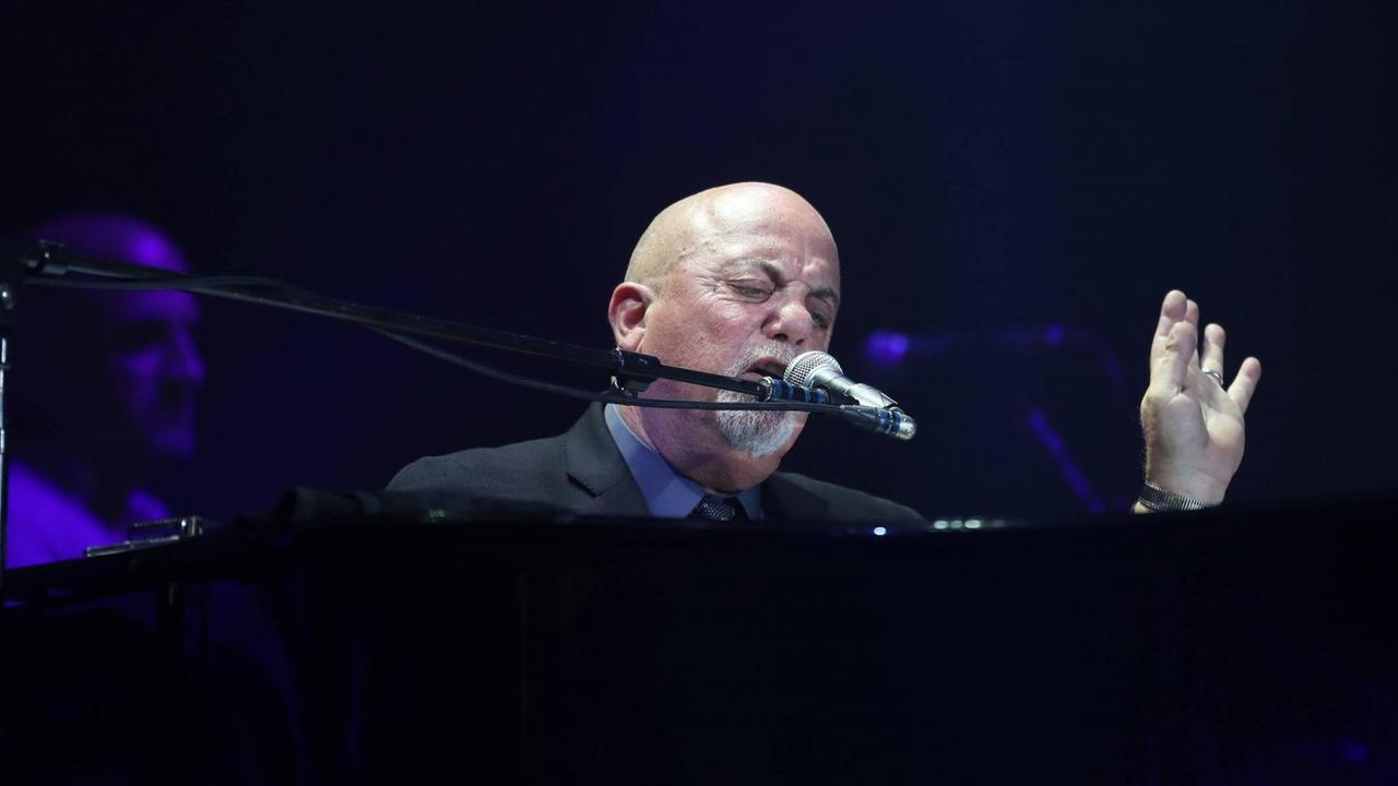 Billy Joel sitzt während eines Konzerts an einem schwarzen Klavier und singt