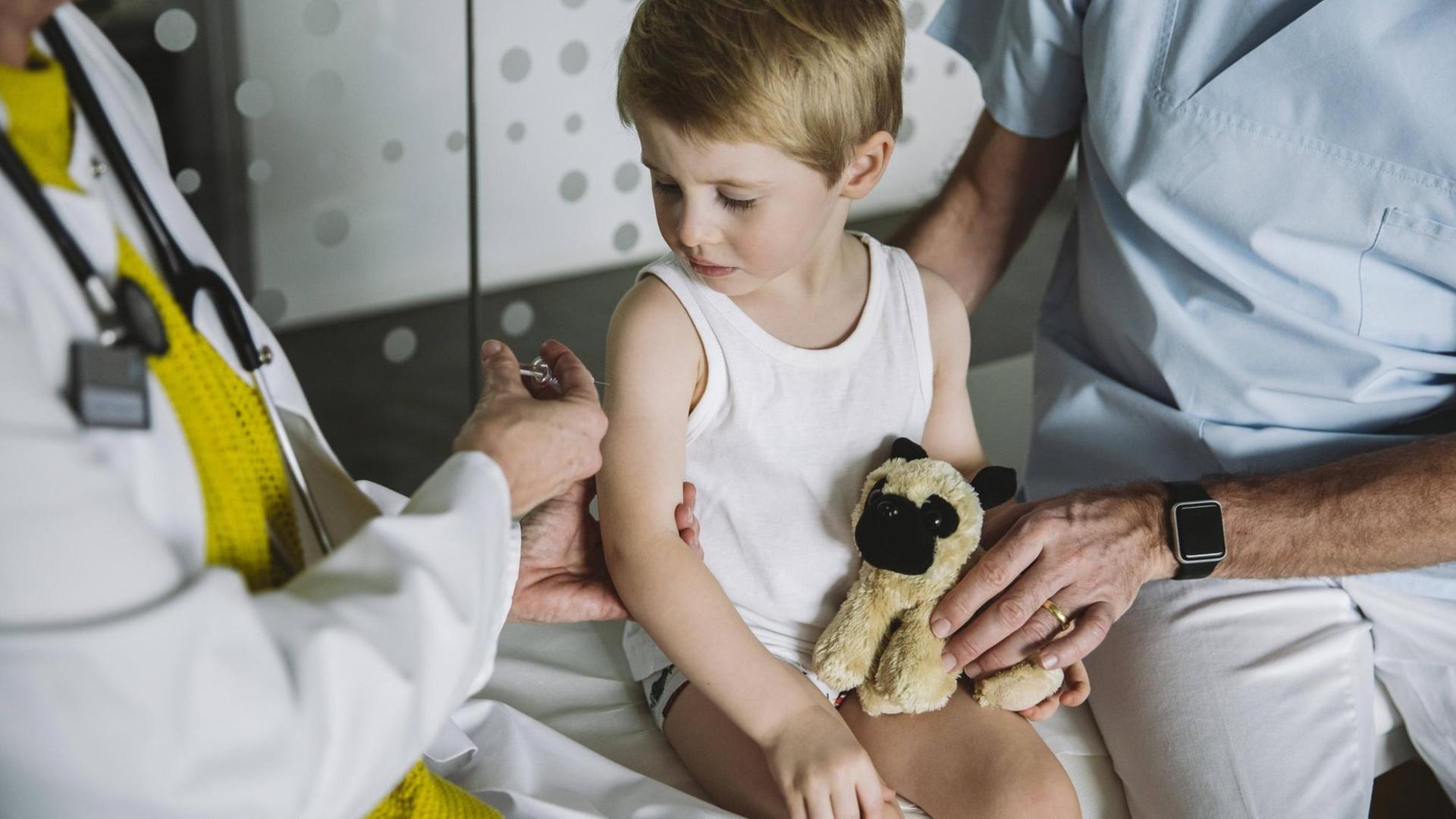 Eine Kinderärztin setzt einem Kleinkind in weißem Unterhemd eine Spritze an den Oberarm. Eine Kinderärztin setzt einem Kleinkind in weißem Unterhemd eine Spritze an den Oberarm.
