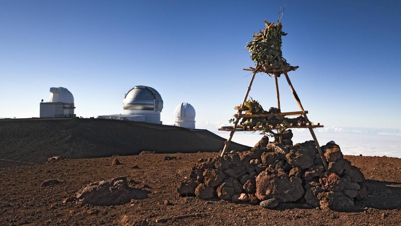 Prähistorische Götterwelt und moderne Wissenschaft: Ein traditioneller hawaiischer Tempel auf dem Gipfel des Vulkans Mauna Kea, im Hintergrund Teile des Mauna Kea-Observatoriums