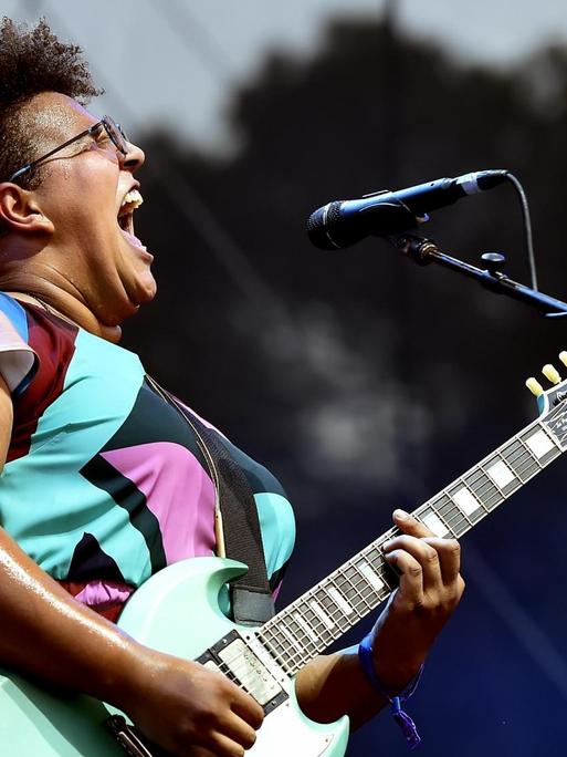 Profilansicht von Brittany Howard mit umgehangener Gitarre singend auf der Bühne.