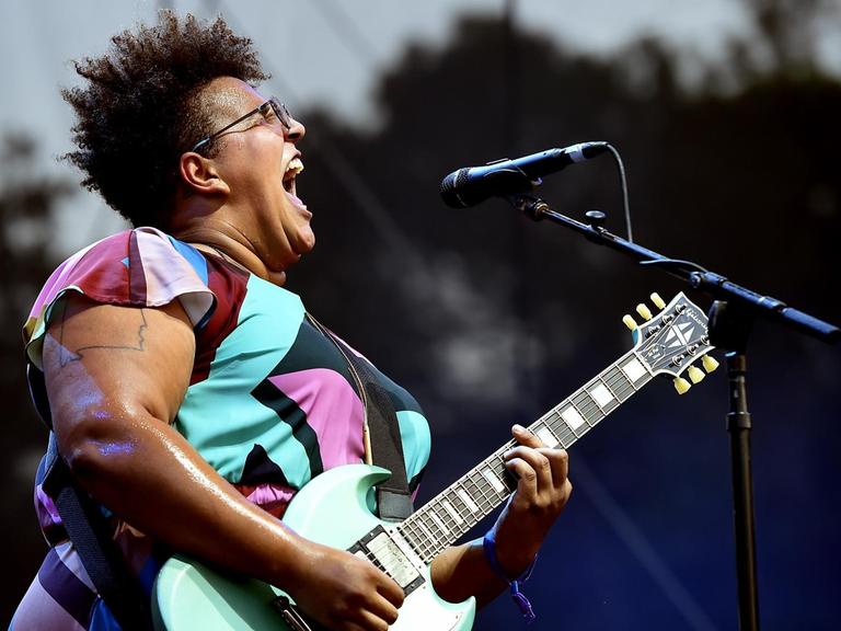 Profilansicht von Brittany Howard mit umgehangener Gitarre singend auf der Bühne.