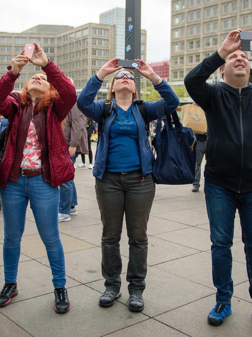 Touristen fotografieren mit ihren Smartphones ein Hochhaus auf dem Alexanderplatz in Berlin.