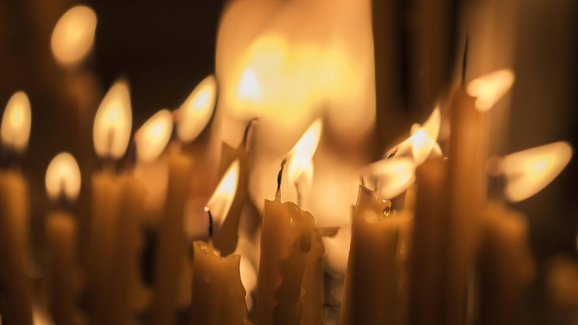 Etliche Kerzen brennen bei leichter Zugluft in einer Kirche.